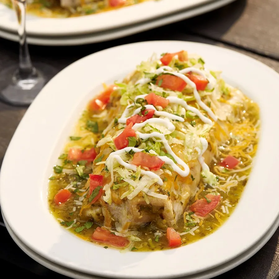 A smothered breakfast burrito under sauce, cheese and fresh garnish