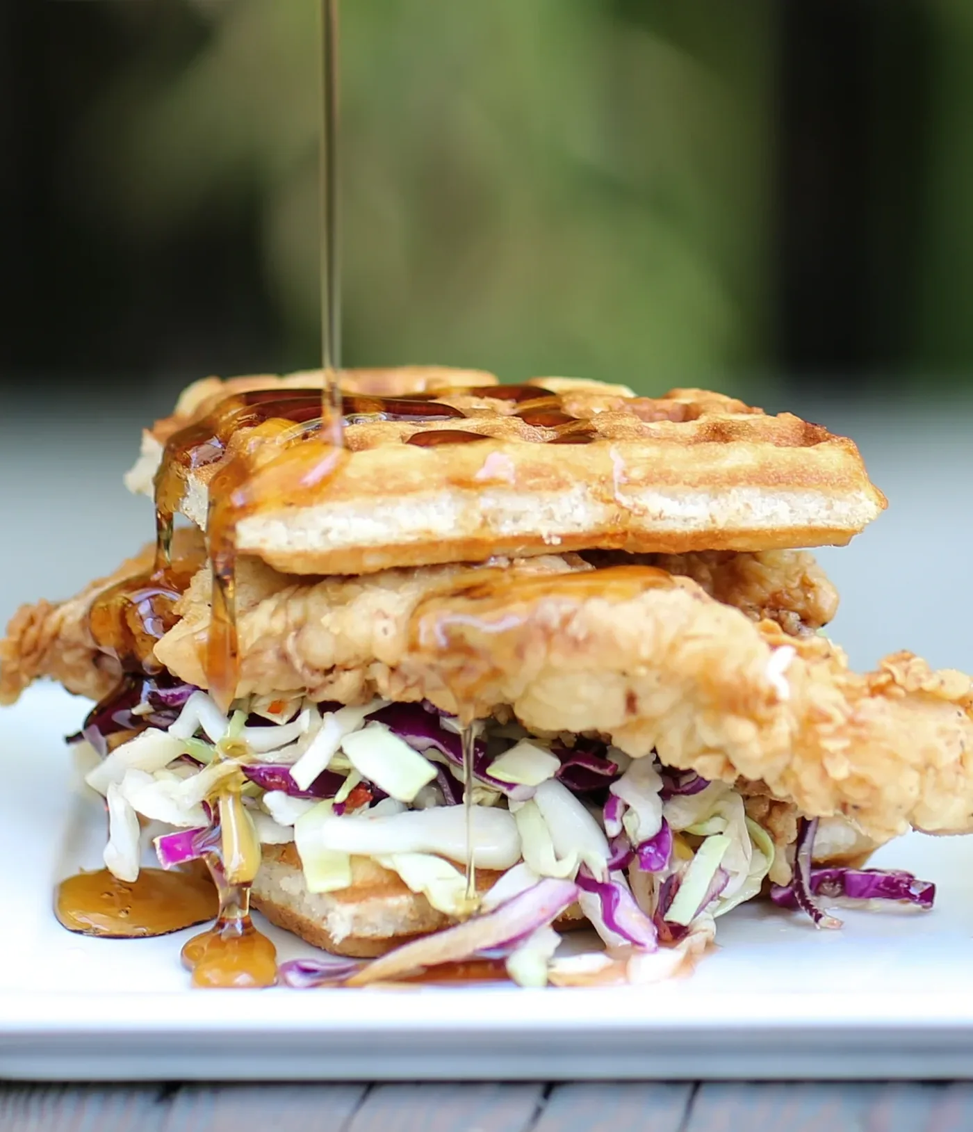 A fried chicken and waffle sandwich stacked with slaw, cut and plated