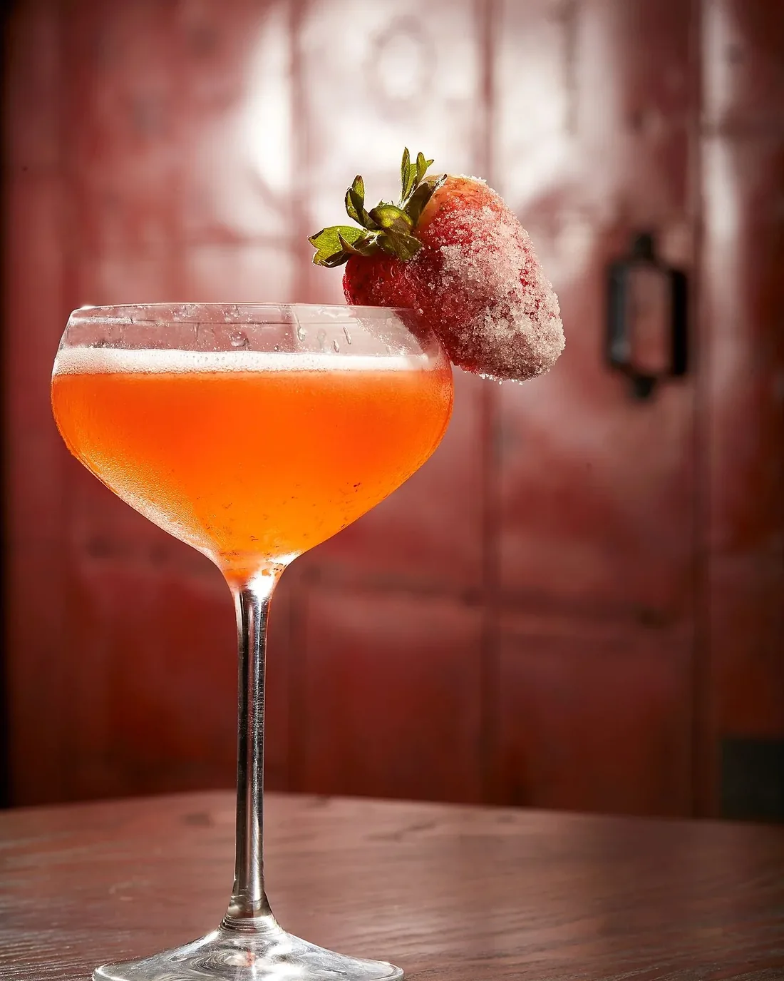 A strawberry cocktail in a coupe glass with a sugared strawberry on the rim