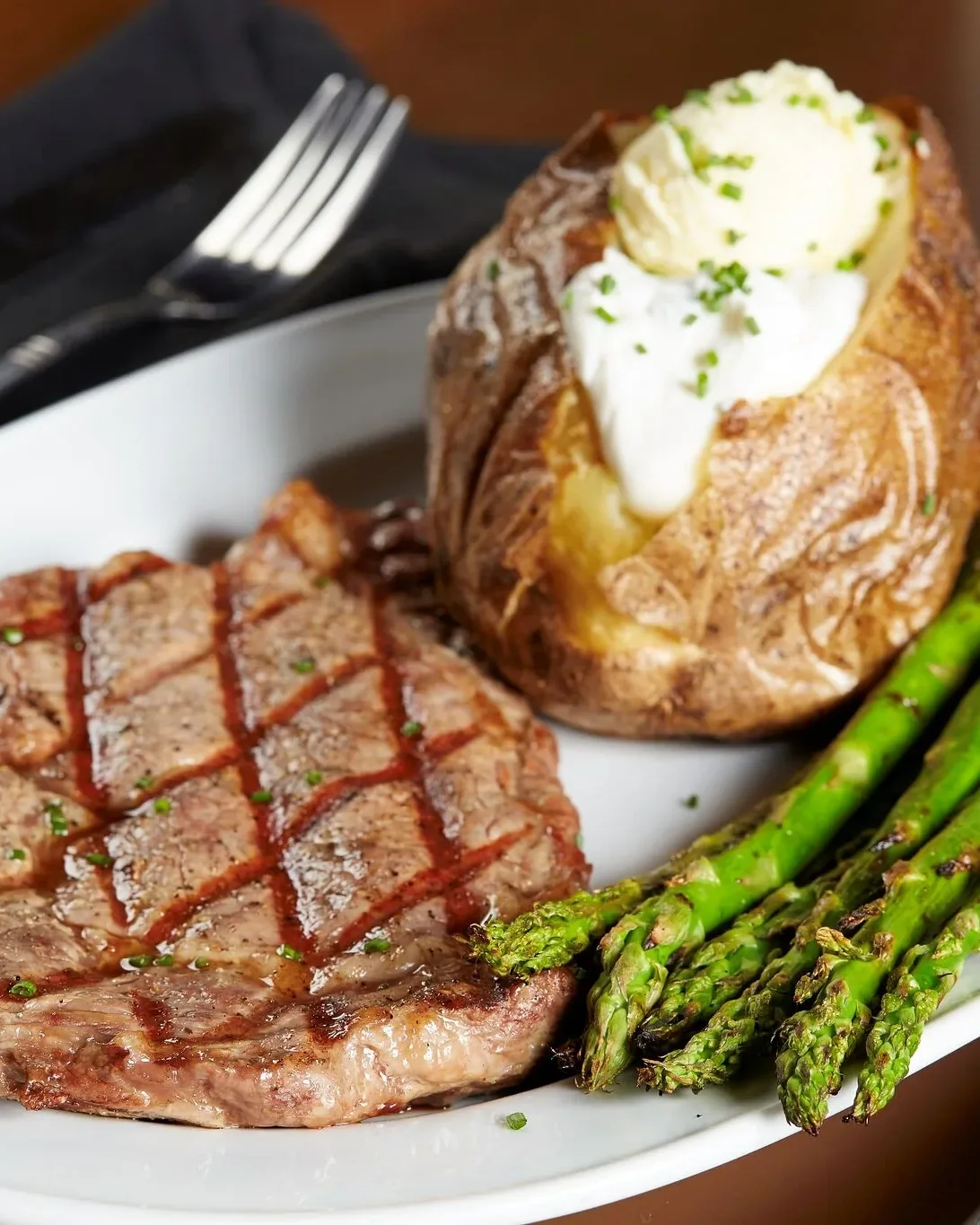 A grilled ribeye steak with a loaded baked potato and grilled asparagus