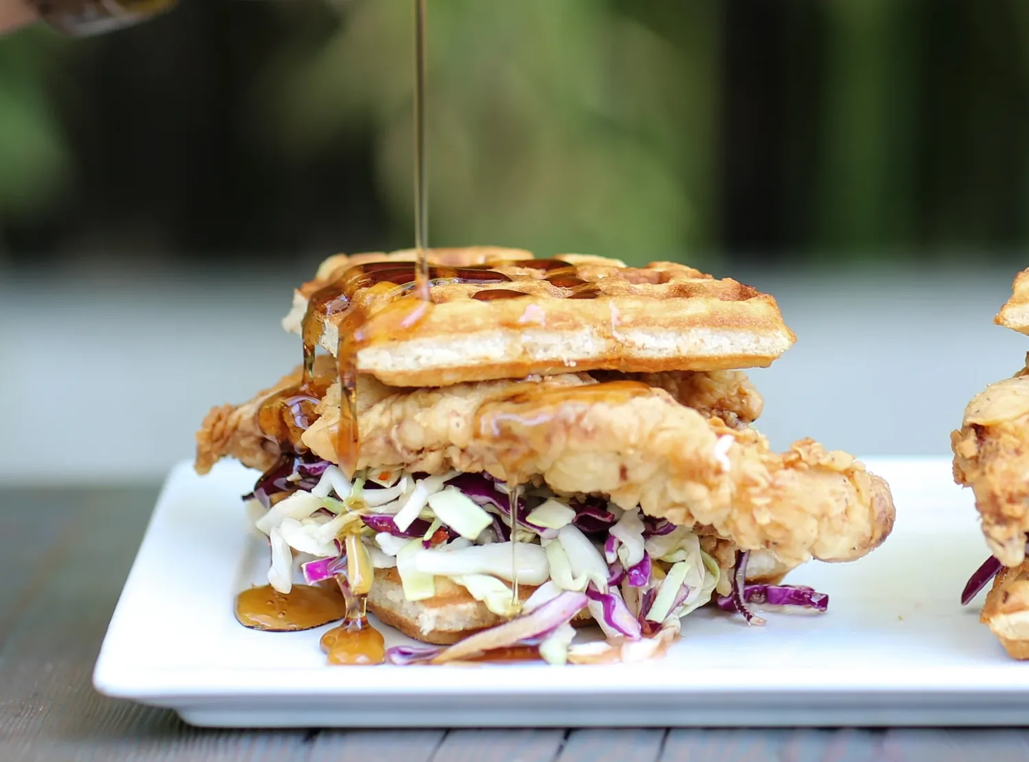 A fried chicken and waffle sandwich with slaw, syrup being poured over it