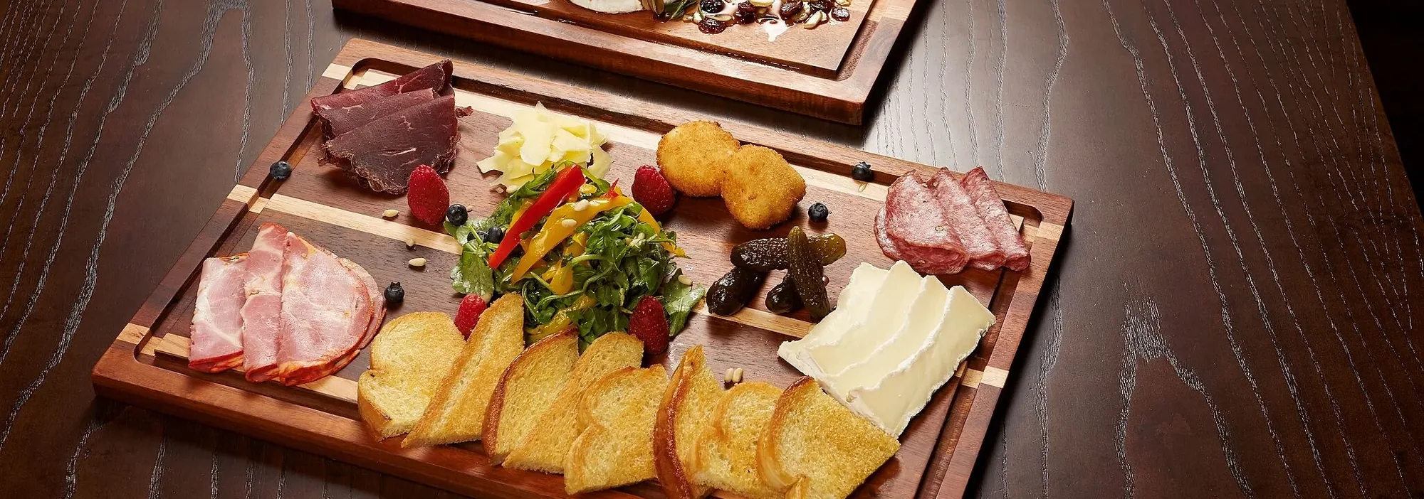 Two wooden boards — a baked brie with fruit and nuts, and a charcuterie board with toast points