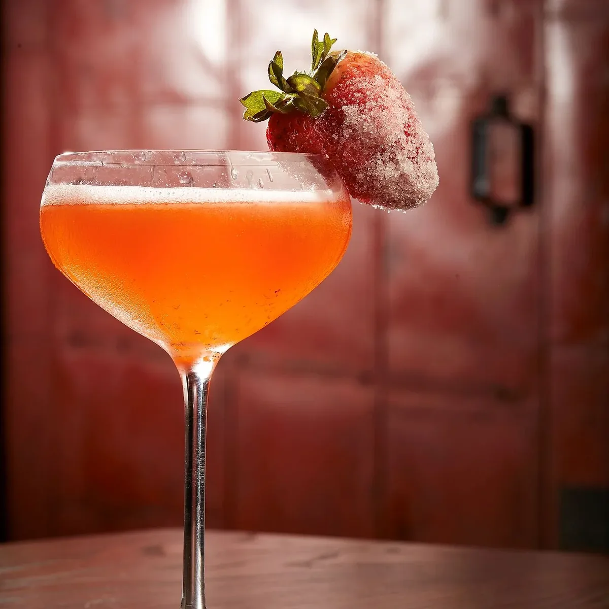 A strawberry cocktail served up in a coupe, rimmed with a sugared strawberry