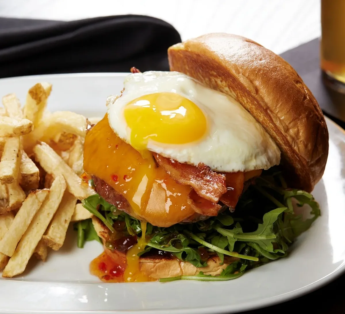 A burger topped with a fried egg, bacon and cheddar, with fries