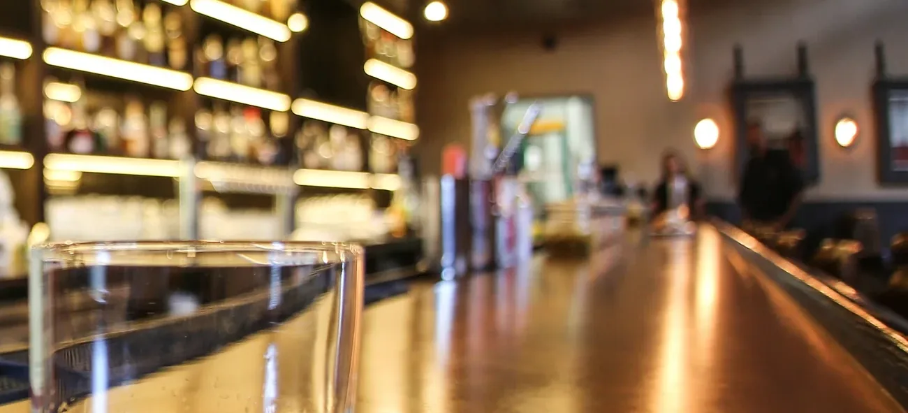 The length of the bar, lit warm, glasses and taps along the counter