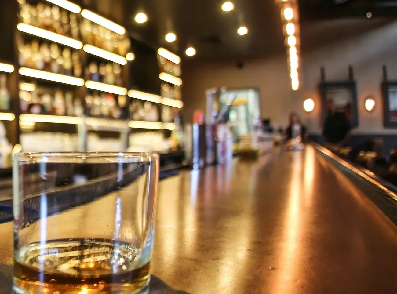 The bar counter stretching away past shelves of backlit bottles