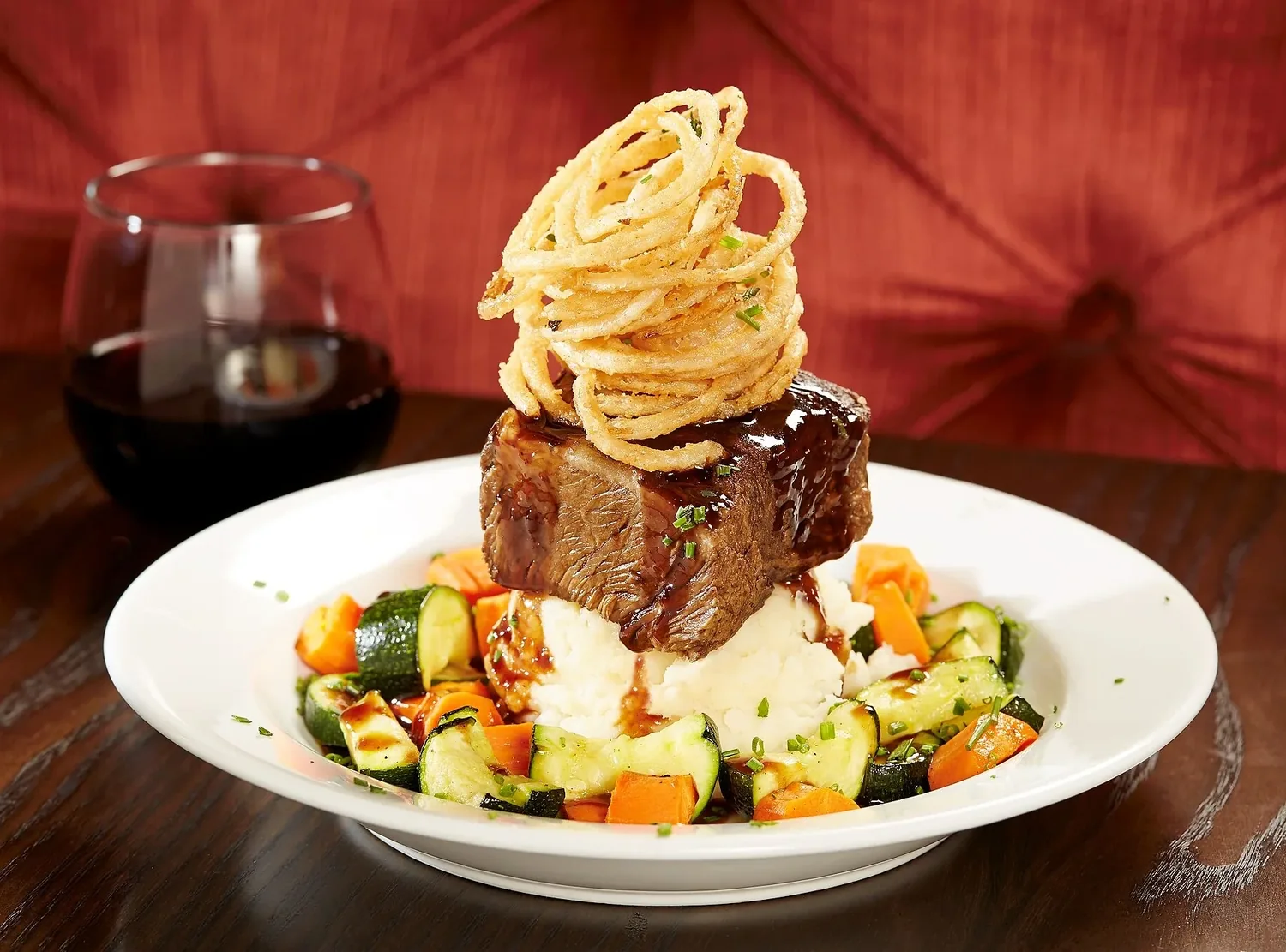 Braised short rib on mashed potatoes with roasted vegetables and crisp onion strings